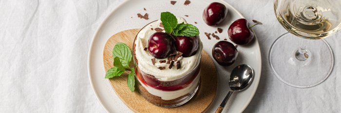 Ein köstliches Dessert in einem Glas, geschichtet mit Sahne, Kirschen und Schokoladenstückchen, garniert mit frischer Minze.