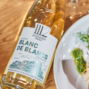 Auf dem Tisch liegt eine Flasche 'Blanc de Blancs', die mit ihrem klaren Design und dem Etikett die Aufmerksamkeit auf sich zieht.