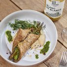 Ein kunstvoll angerichteter Teller mit Wraps, die mit Spargel gefüllt sind, und einer Beilage aus cremigem Hummus.