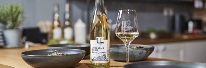 Ein eleganter Tisch mit einer Flasche Gutedel und Grau Burgunder, umgeben von stilvollen Schalen mit frischen Zutaten.