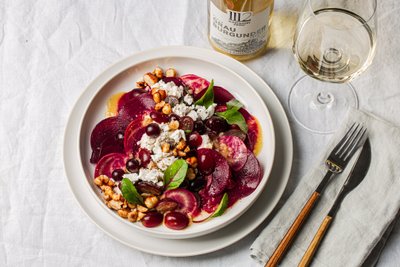 Ein kunstvoll angerichteter Salat mit Rote Bete, Trauben, Nüssen und frischen Kräutern auf einem weißen Teller.