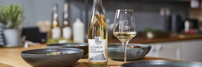 Ein eleganter Tisch mit einer Flasche Gutedel und Grau Burgunder, umgeben von stilvollen Schalen mit frischen Zutaten.