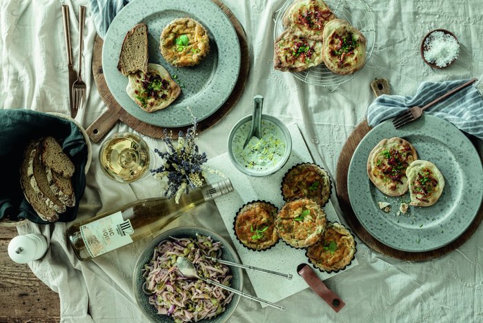 Ein rustikaler Tisch mit verschiedenen Gerichten, darunter herzhafte Tartes, frisches Brot und ein Glas Weißwein.