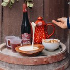 Ein roter Glühwein in einer dekorativen Kanne steht neben einer Schüssel mit geschmolzenem Käse und knusprigem Brot.