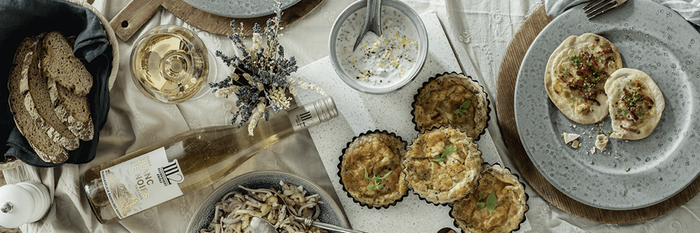Ein rustikaler Tisch mit verschiedenen Gerichten, darunter herzhafte Quiches, frisches Brot und ein Glas Weißwein.