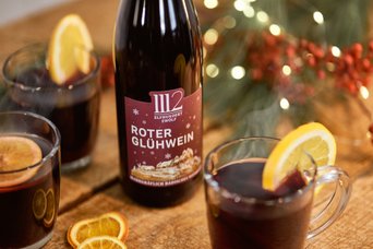 Ein Flasche Roten Glühwein steht neben zwei Gläsern, die mit Zitrone dekoriert sind, auf einem rustikalen Holztisch.