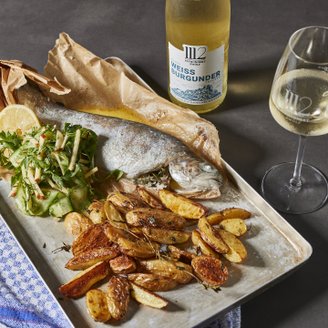 Ein Teller mit gebratenem Fisch, knusprigen Kartoffeln und einem frischen Salat aus Gurken und Kräutern, garniert mit Zitrone.