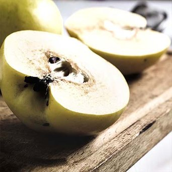 Zwei halbierte Äpfel liegen auf einem Holzbrett, mit sichtbaren Kernen und einer glatten, gelben Schale.