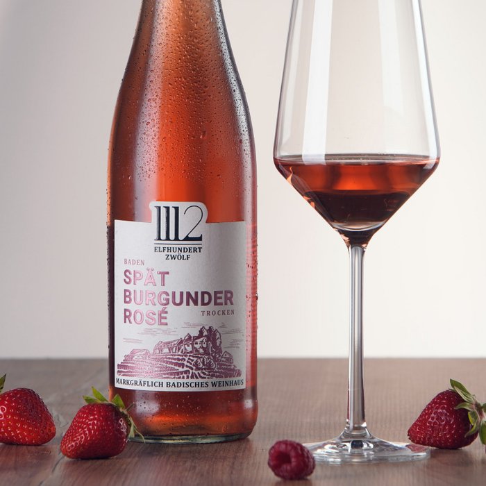 Eine Flasche Spätburgunder Rosé steht neben einem eleganten Weinglas, umgeben von frischen Erdbeeren und Himbeeren.