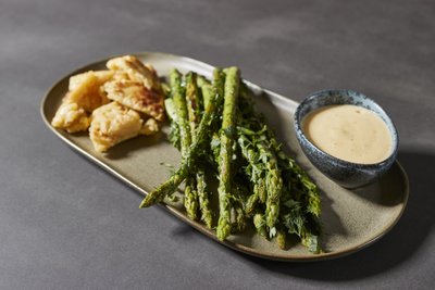 Ein appetitliches Gericht mit grünem Spargel, knusprigen Teigstücken und einer cremigen Sauce in einer dekorativen Schale.
