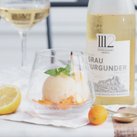 Das Sorbet in einem Kristallglas wird von Zitronen- und Kumquatstücken sowie einem Glas Weißwein begleitet.