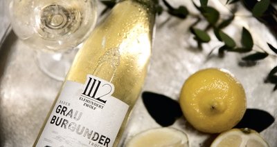 Ein Glas Weißwein und eine Flasche Grau Burgunder sind auf einem silbernen Tablett platziert, umgeben von Zitronen.