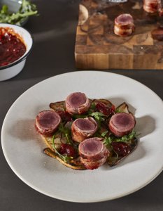 Auf einem weißen Teller liegen mehrere Rinderfiletstücke, umgeben von gegrilltem Gemüse und einer fruchtigen Sauce.