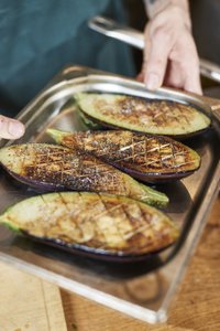 Gegrillte Auberginenhälften auf einem silbernen Tablett, mit einer knusprigen Oberfläche und Gewürzen bestreut.