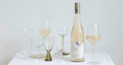 Ein eleganter Tisch mit einer Flasche Blanc de Noirs und verschiedenen Gläsern, die auf einem weißen Tuch arrangiert sind.