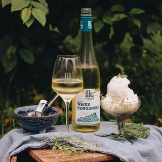 Ein Glas mit Weißwein und eine Flasche stehen neben einer eleganten Schale mit Sorbet, alles auf einem blauen Tuch drapiert.