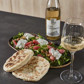 Ein gedeckter Tisch mit einem gesunden Salat, Fladenbrot und einer Flasche Grau Burgunder, ideal für ein entspanntes Essen.