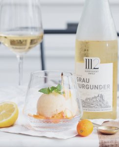 Das Sorbet in einem Kristallglas wird von Zitronen- und Kumquatstücken sowie einem Glas Weißwein begleitet.