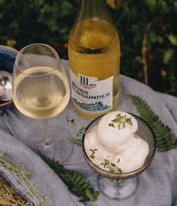 Ein elegantes Glas Weißwein steht neben einer Schale mit cremigem Sorbet, garniert mit frischen Kräutern.