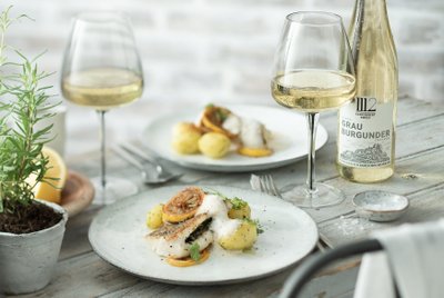 Ein elegantes Gericht mit gebratenem Fisch, Kartoffeln und Zitronenscheiben, serviert auf einem weißen Teller.