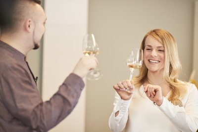 Ein Mann und eine Frau stoßen mit Weingläsern an, während sie lächeln und eine fröhliche Atmosphäre genießen.