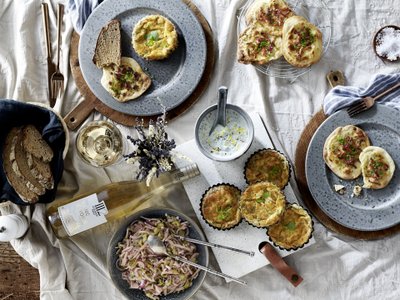 Ein rustikaler Tisch mit verschiedenen Gerichten, darunter herzhafte Quiches, frisches Brot und ein Glas Weißwein.