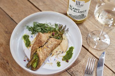 Ein kunstvoll angerichteter Teller mit Wraps, die mit Spargel gefüllt sind, und einer Beilage aus cremigem Hummus.