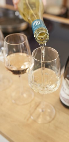 Wein wird in ein elegantes Glas gegossen, während die Flasche und andere Gläser auf einem hellen Holztisch arrangiert sind.