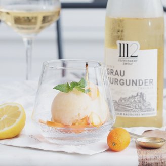 Das Sorbet in einem Kristallglas wird von Zitronen- und Kumquatstücken sowie einem Glas Weißwein begleitet.