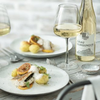 Ein elegantes Gericht mit gebratenem Fisch, Kartoffeln und Zitronenscheiben, serviert auf einem weißen Teller.