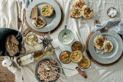 Ein rustikaler Tisch mit verschiedenen Gerichten, darunter herzhafte Quiches, frisches Brot und ein Glas Weißwein.