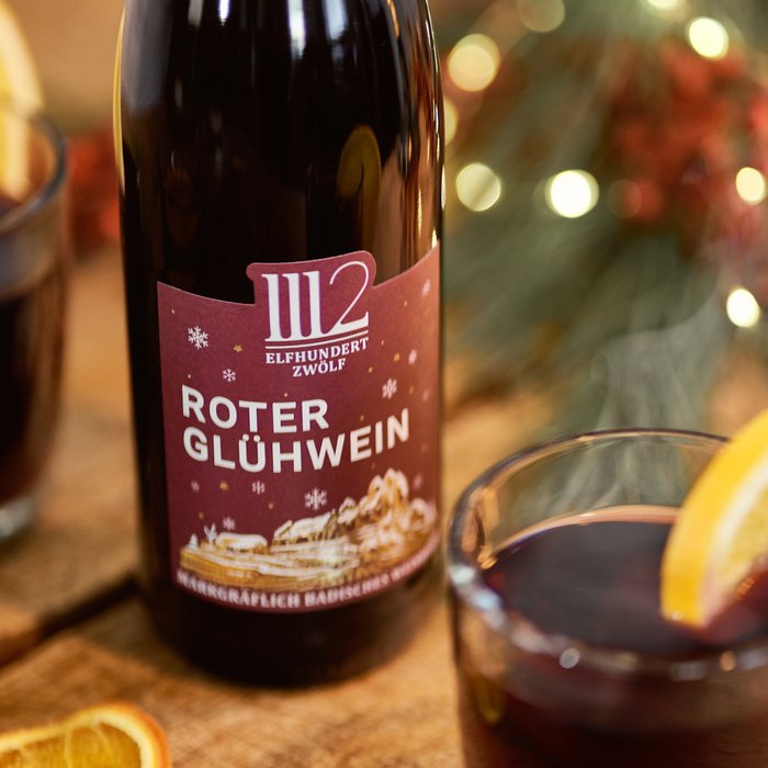 Ein Flasche Roten Glühwein steht neben zwei Gläsern, die mit Zitrone dekoriert sind, auf einem rustikalen Holztisch.