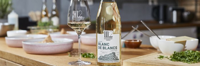 Ein elegantes Glas Weißwein steht neben einer Flasche 'Blanc de Blancs' auf einem Holzarbeitsplatz in einer modernen Küche.