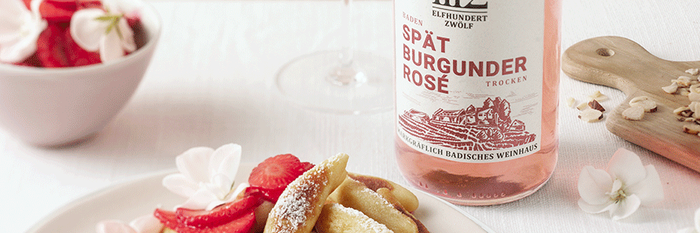 Ein köstliches Dessert aus gebratenen Teigstücken und Erdbeeren, dekoriert mit Blüten, serviert mit einem Glas Spätburgunder Rosé.