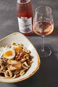 Ein Teller mit einer bunten Mischung aus Nudeln, Eiern, Nüssen und Pilzen, begleitet von einem Glas Roséwein.