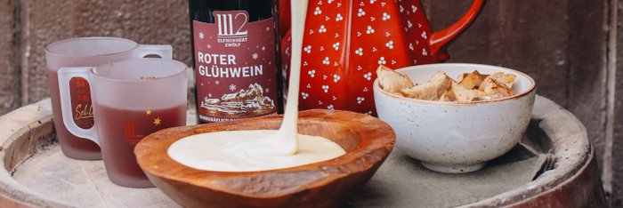 Ein roter Glühwein in einer dekorativen Kanne steht neben einer Schüssel mit geschmolzenem Käse und knusprigem Brot.