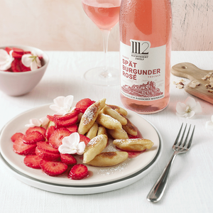 Ein köstliches Dessert aus gebratenen Teigstücken und Erdbeeren, dekoriert mit Blüten, serviert mit einem Glas Spätburgunder Rosé.