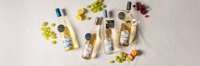 Ein stilvolles Arrangement von Weinen mit Gold- und Silbermedaillen, umgeben von saftigen Trauben und Zitrusfrüchten auf einem Tisch.