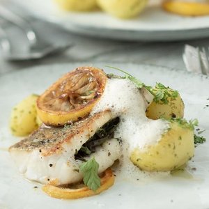 Ein zartes Stück gebratenen Fischs, garniert mit Zitronenscheiben und frischen Kräutern, serviert mit Kartoffeln.