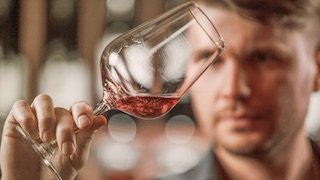 Ein Mann betrachtet aufmerksam ein Glas mit roséfarbenem Wein, während er in einer stilvollen Umgebung steht.