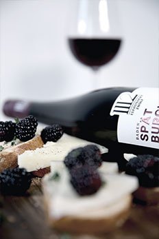 Ein elegantes Arrangement aus frischem Brot, Käse und Brombeeren, begleitet von einer Flasche Spätburgunder und einem Glas Rotwein.