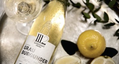 Ein Glas Weißwein und eine Flasche Grau Burgunder sind auf einem silbernen Tablett platziert, umgeben von Zitronen.