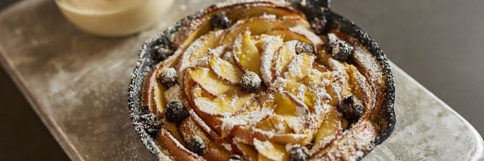 Ein appetitlicher Obstkuchen mit dünn geschnittenen Äpfeln und Heidelbeeren, auf einem silbernen Blech präsentiert.