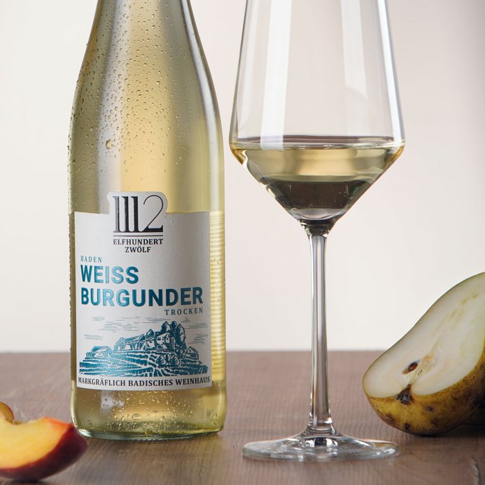 Eine Flasche Weißburgunder steht neben einem Glas Wein und frischen Früchten auf einem Holzuntergrund.