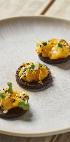 Ein Teller mit drei kleinen, runden Snacks, die mit einer leuchtend gelben Creme und zarten grünen Sprossen geschmückt sind.