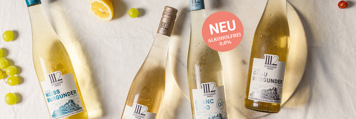 Stilvoll arrangierte Früchte und Weinflaschen mit den Etiketten 'Weißburgunder', 'Blanc de Noirs', 'Grau Burgunder' und 'Blanc Zéro'.