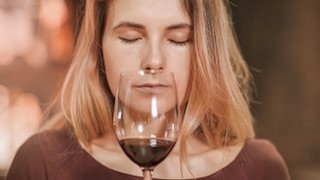 Die Frau mit langen, blonden Haaren schließt die Augen und konzentriert sich auf den aromatischen Duft des Weins in ihrem Glas.