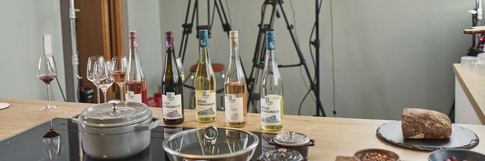 Ein einladender Kochplatz mit Weinen, einem Topf und Snacks, umgeben von Kameras für eine bevorstehende Aufnahme.