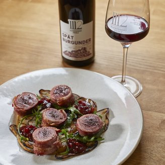 Ein stilvolles Dinner-Arrangement mit Rehrücken und einem Glas Spätburgunder auf einem Holztisch.