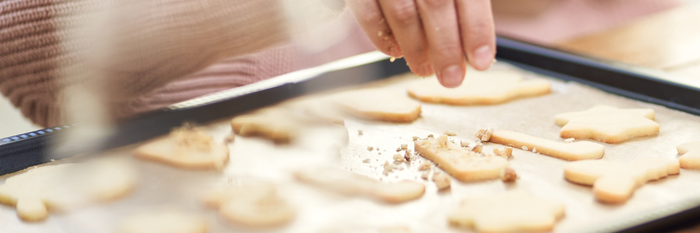 Eine Frau in einem rosa Pullover streut Zucker über frisch gebackene Plätzchen auf einem Backblech.